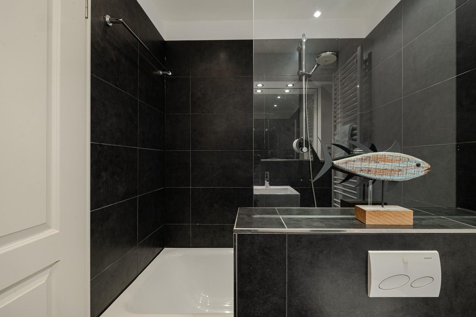 Badezimmer mit Dusche, Waschbecken und dekorativer Fischskulptur.