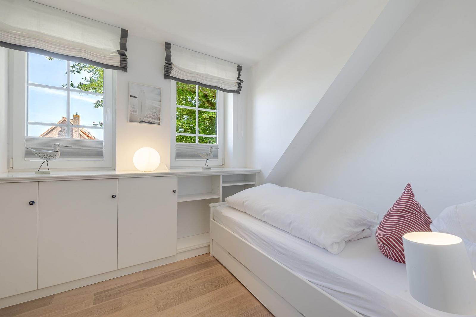 Schlafzimmer mit Dachschräge, zwei Fenstern, Bett und Schrank.