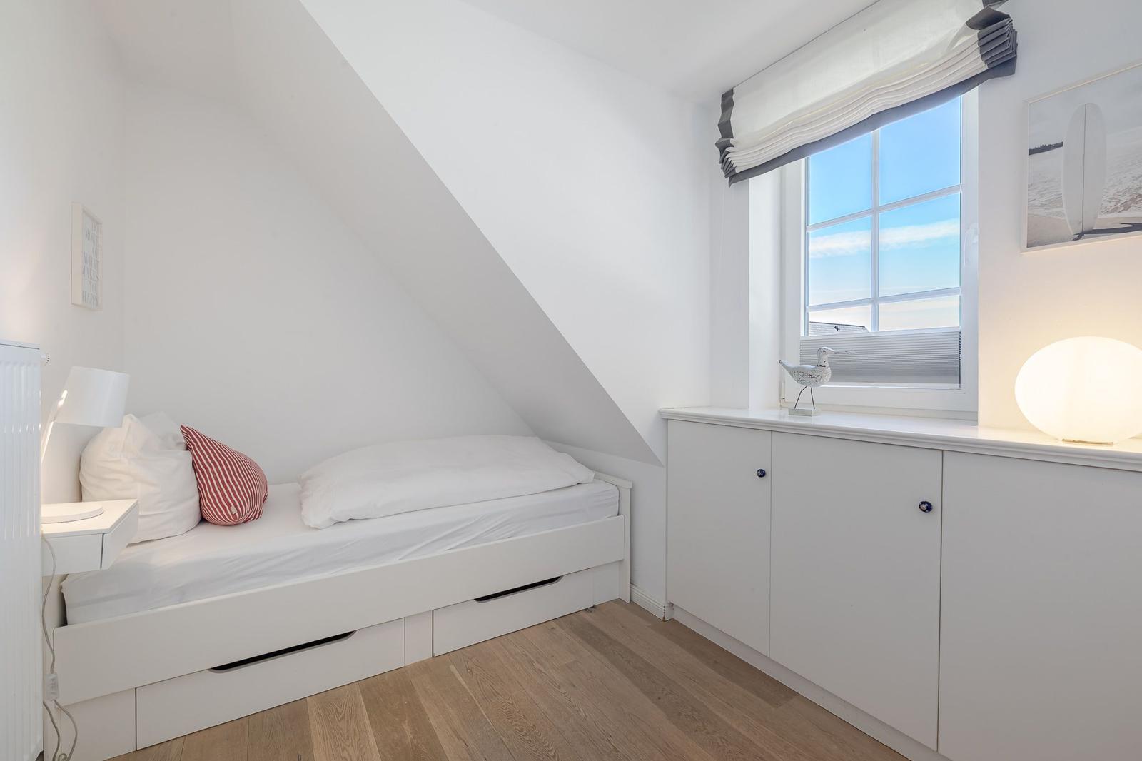 Kleines Schlafzimmer mit Dachschräge, weißem Bett und Fenster mit Blick.