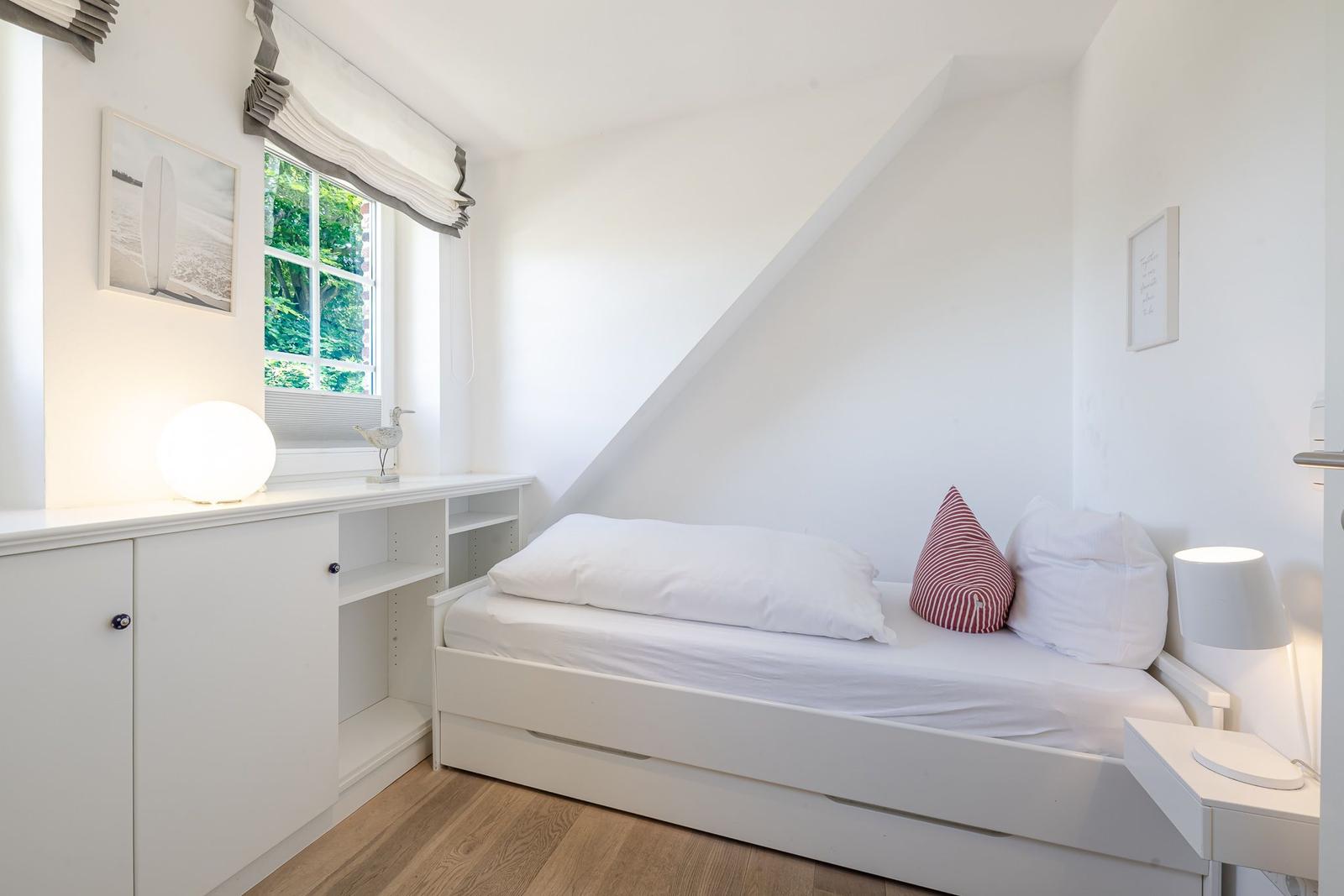 Schlafzimmer mit weißem Bett, Fenster und Schrank.