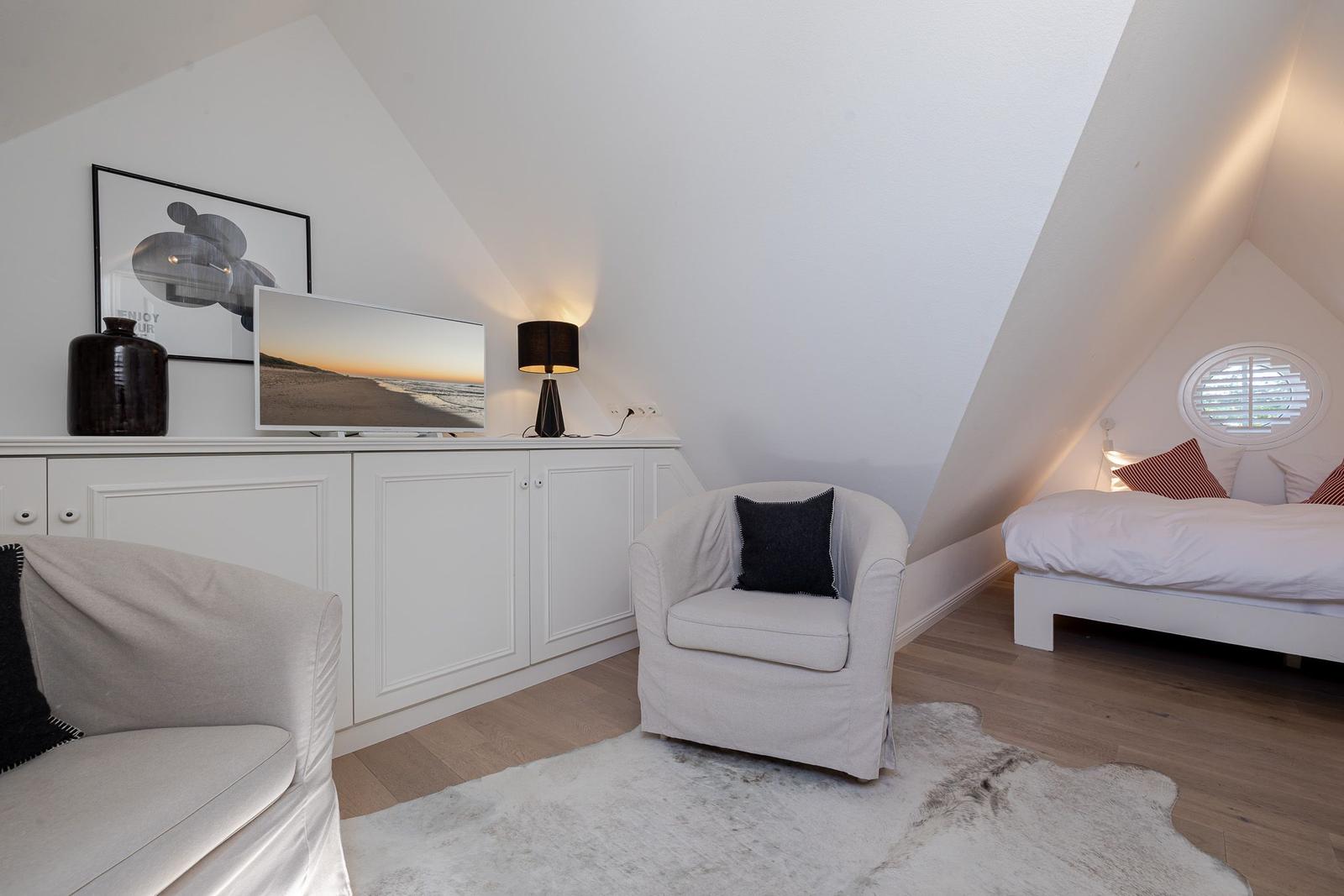 Schlafzimmer mit Dachschrägen, Bett, Sessel und Fernseher auf Schrank.