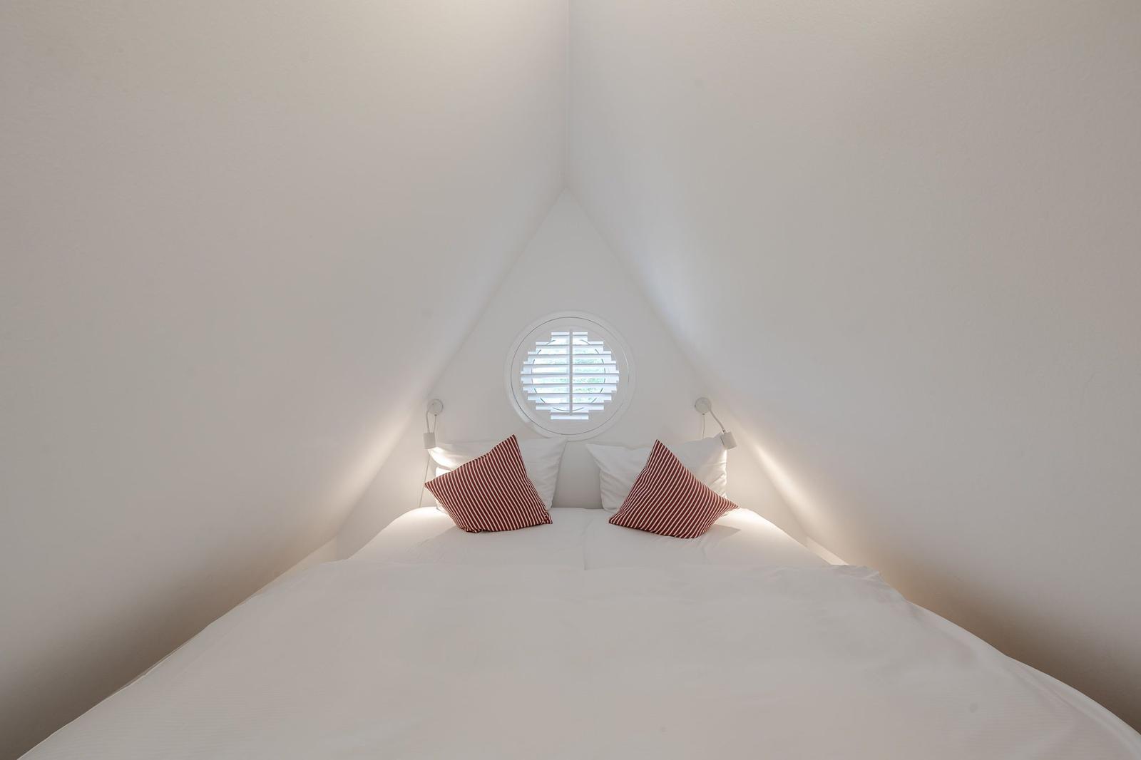Schlafzimmer mit Dachfenster und Bett unter Dachschräge.