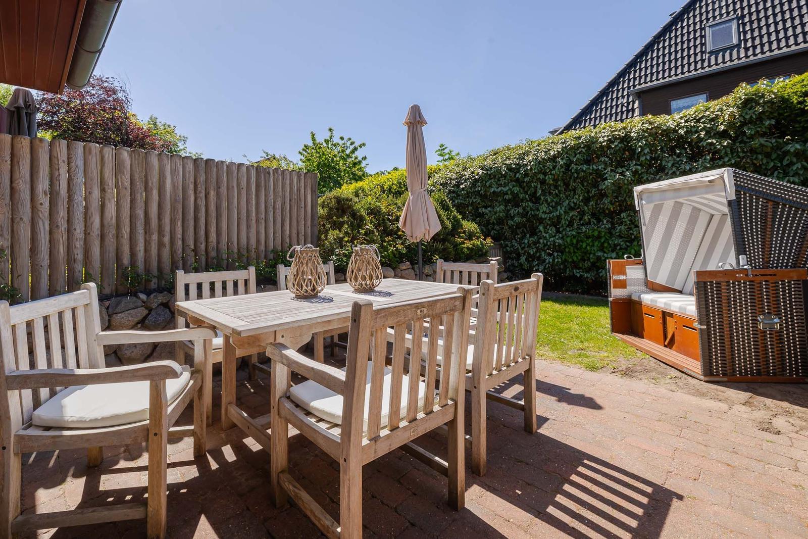 Terrasse mit Holztisch, Stühlen und Sonnenschirm. Gartenhaus und Hedges sind sichtbar.