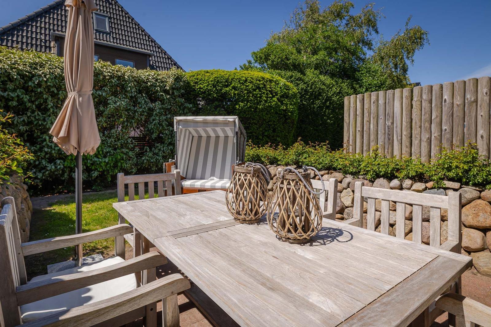 Holztisch mit Stühlen, Sonnenschirm und Strandkorb im Garten.
