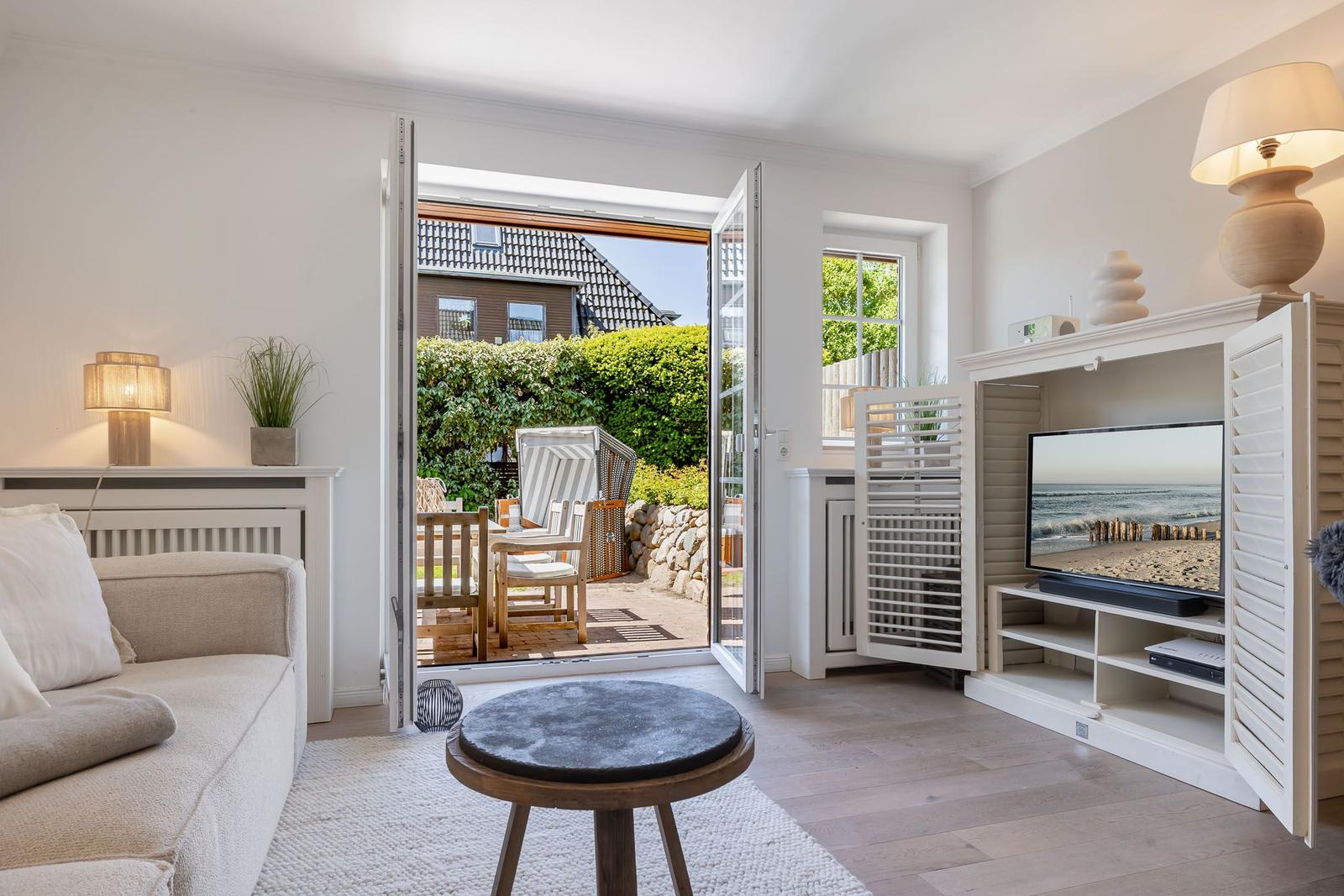 Wohnzimmer mit offenem Balkon, Sofa, Fernseher und TV-Schrank.