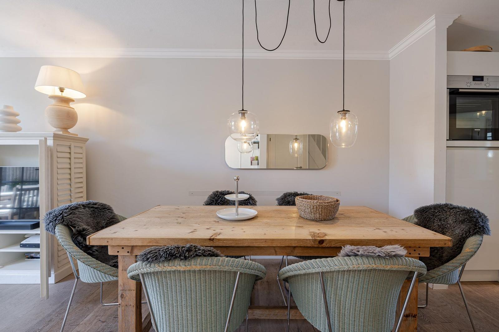 Holztisch mit Stühlen, Pendelleuchten und Spiegel an der Wand.