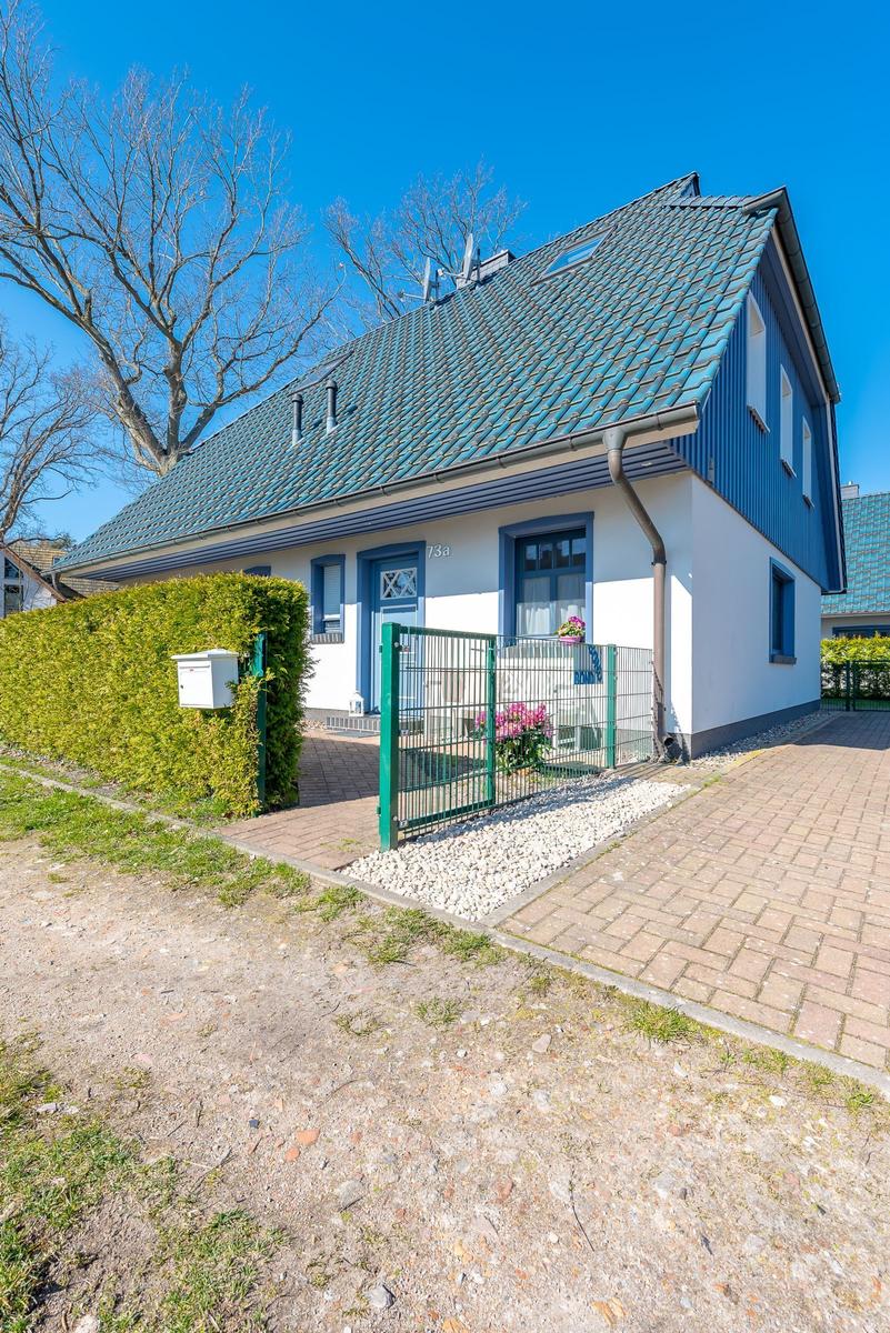 Haus mit blauem Dach und weißer Fassade, grüner Zaun und gepflasterter Weg.
