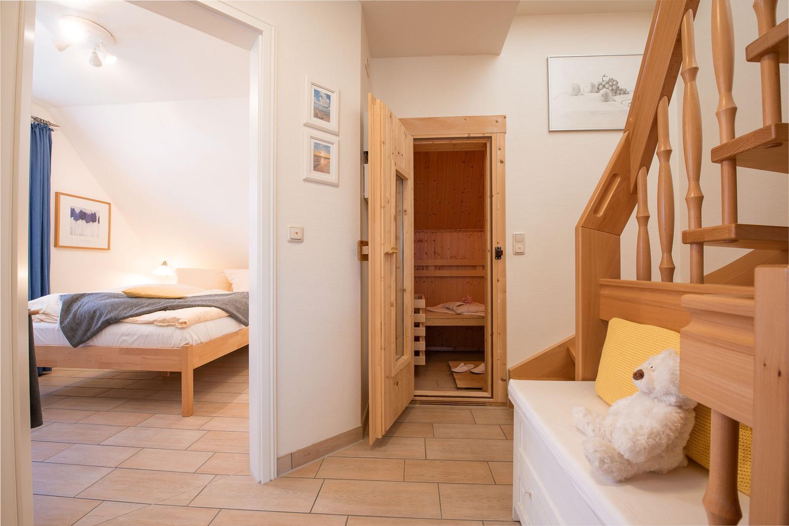 Schlafzimmer mit Bett, Sauna und Holztreppe mit Teddybärenbank.