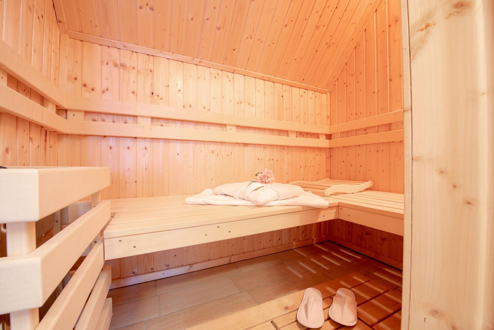 Sauna mit Holzbank, Handtuch und Blume. Holzfußboden und Schuhe.