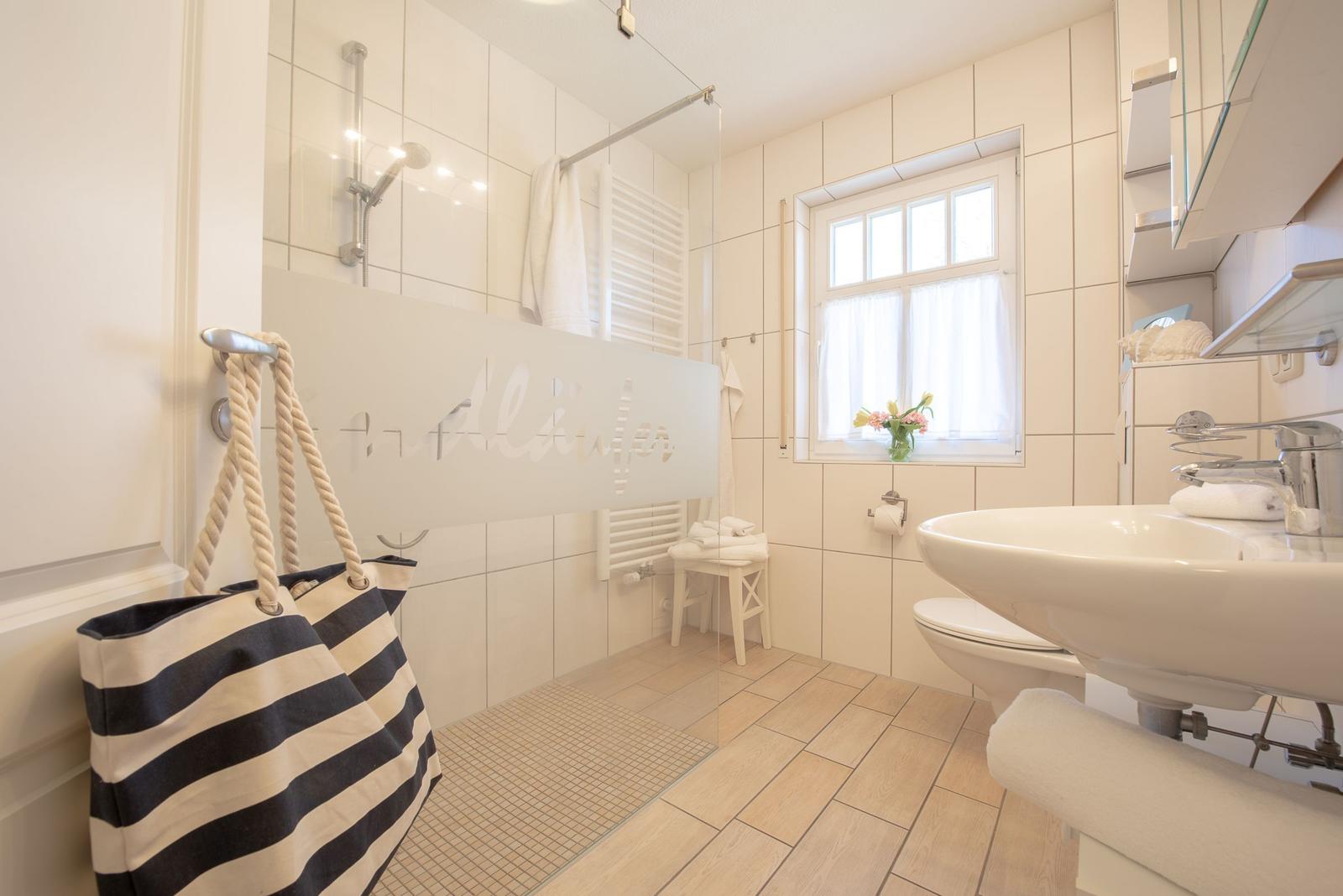 Badezimmer mit Dusche, Waschbecken und Fenster mit Blumen.