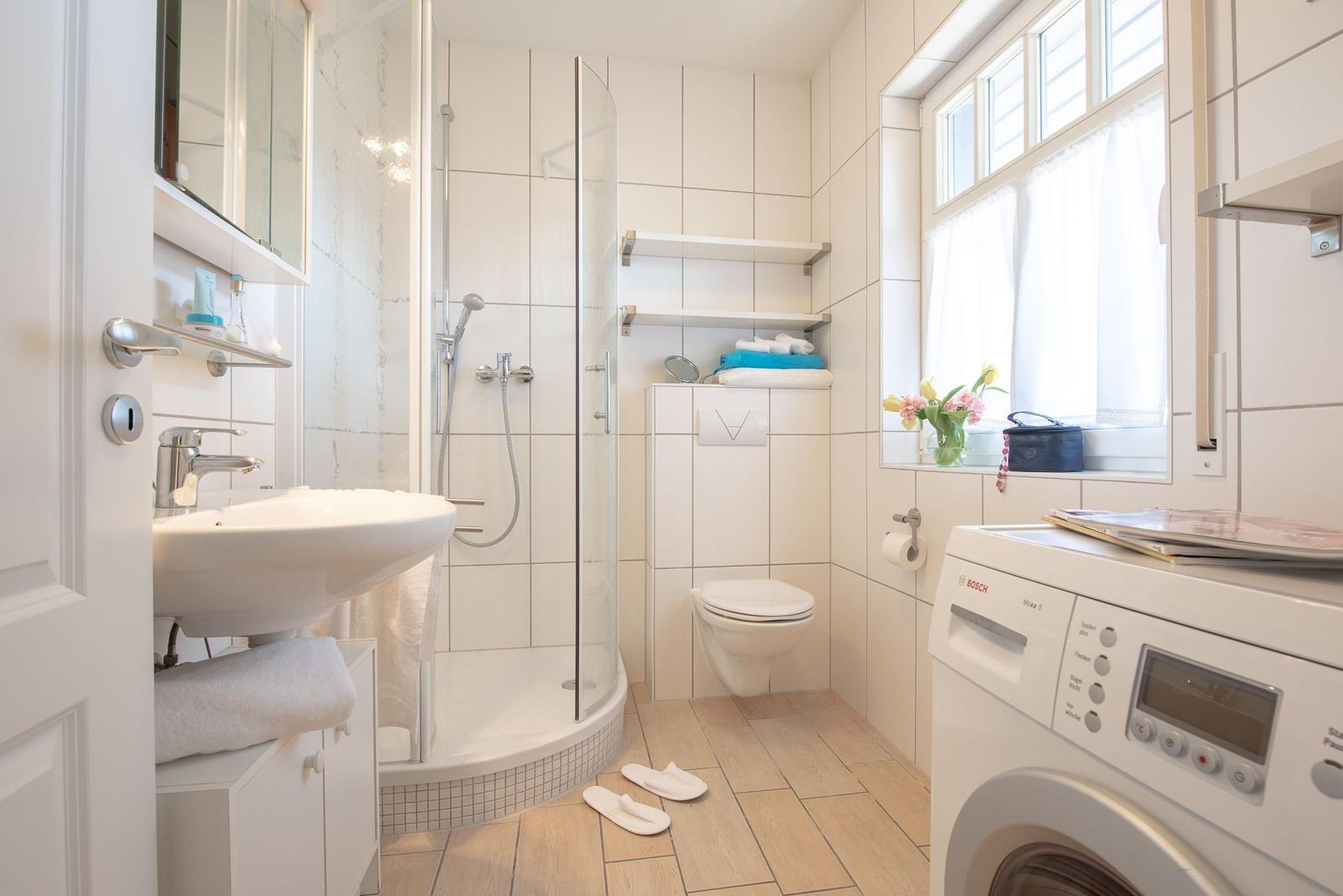 Badezimmer mit Dusche, Waschbecken, Toilette und Waschmaschine.
