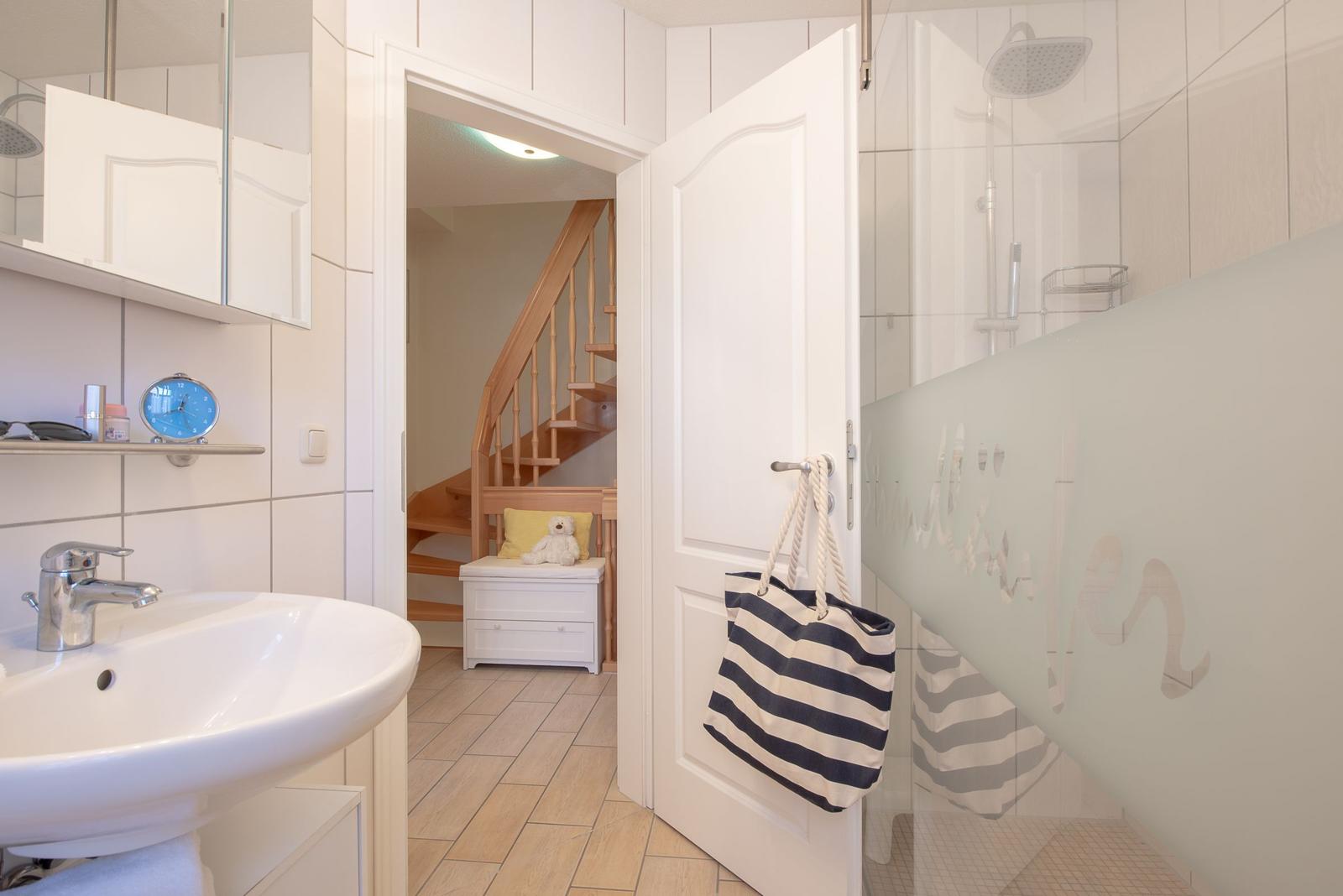 Badezimmer mit Dusche, Waschbecken und Blick in die Treppe.