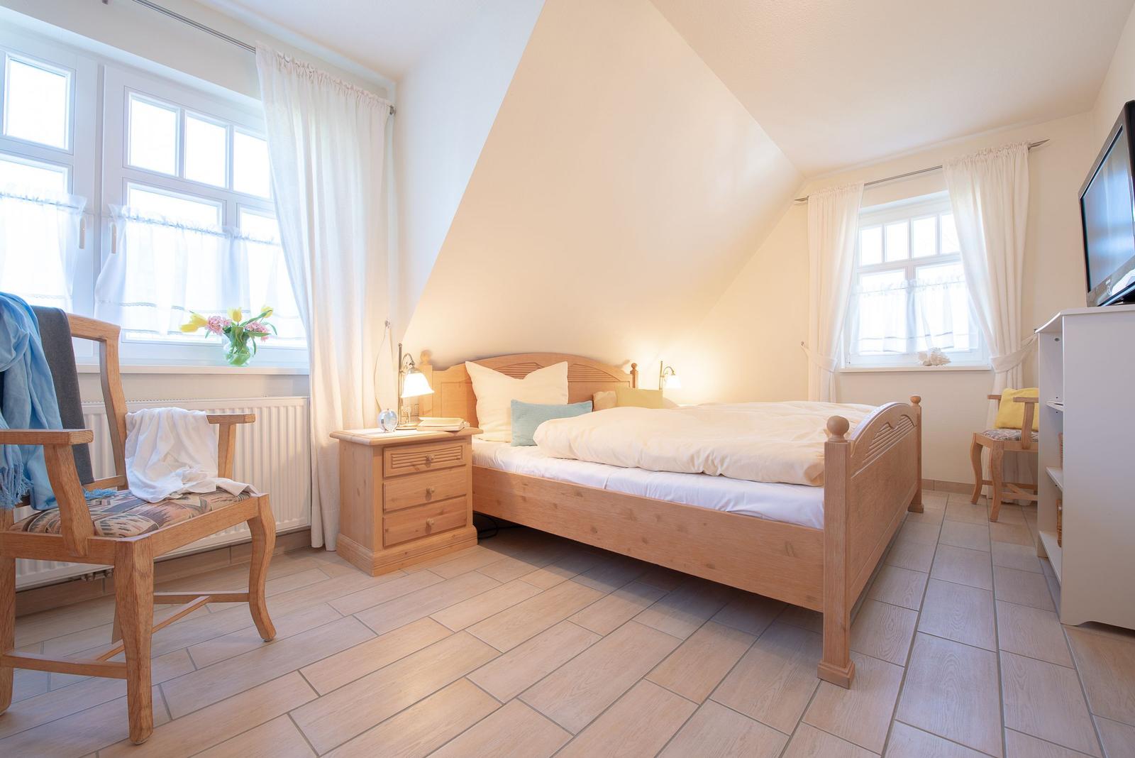 Schlafzimmer mit Holzbett, zwei Fenstern und TV-Schrank.