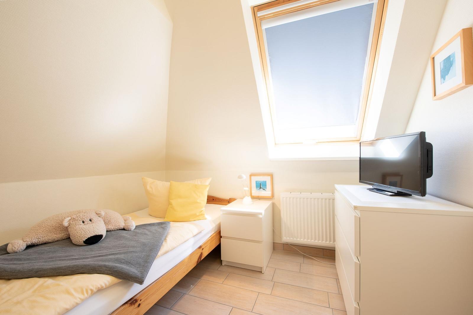 Schlafzimmer mit Dachschrägen, Bett, Nachttisch, Fernseher und Dachfenster.