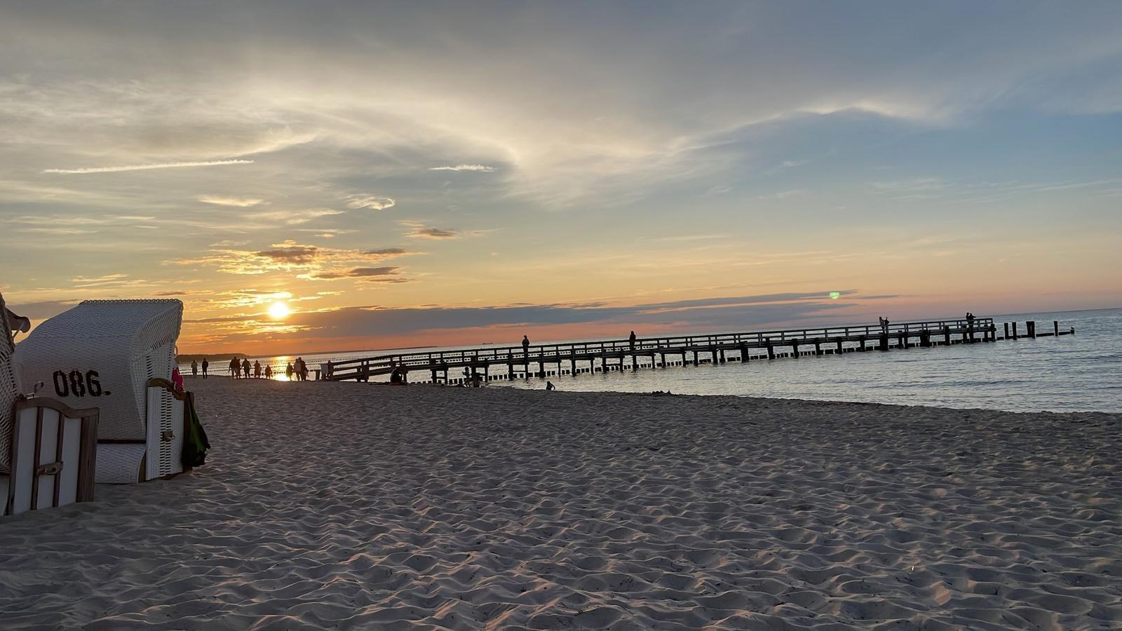 Sonnenuntergang am Strand mit Steg und Strandkorb.