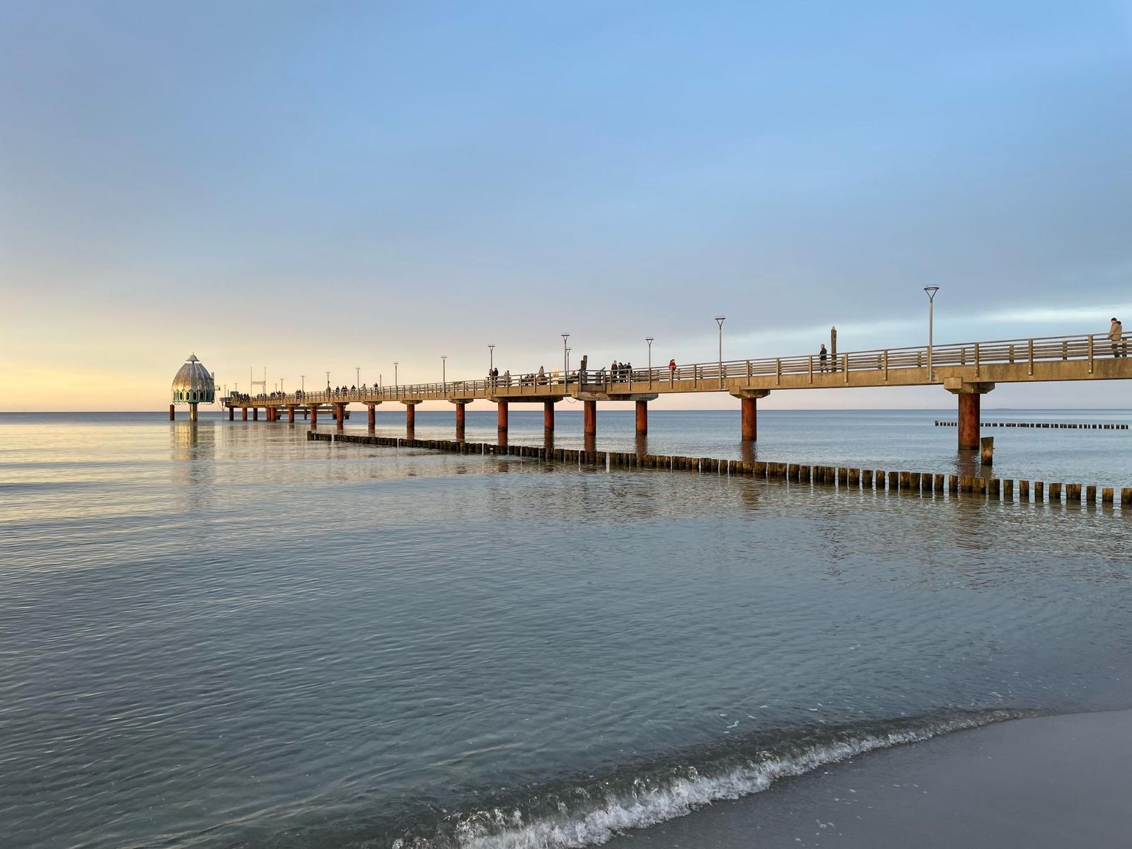 Langgezogener Steg führt ins Meer, mit Personen und einer Kuppel am Ende.