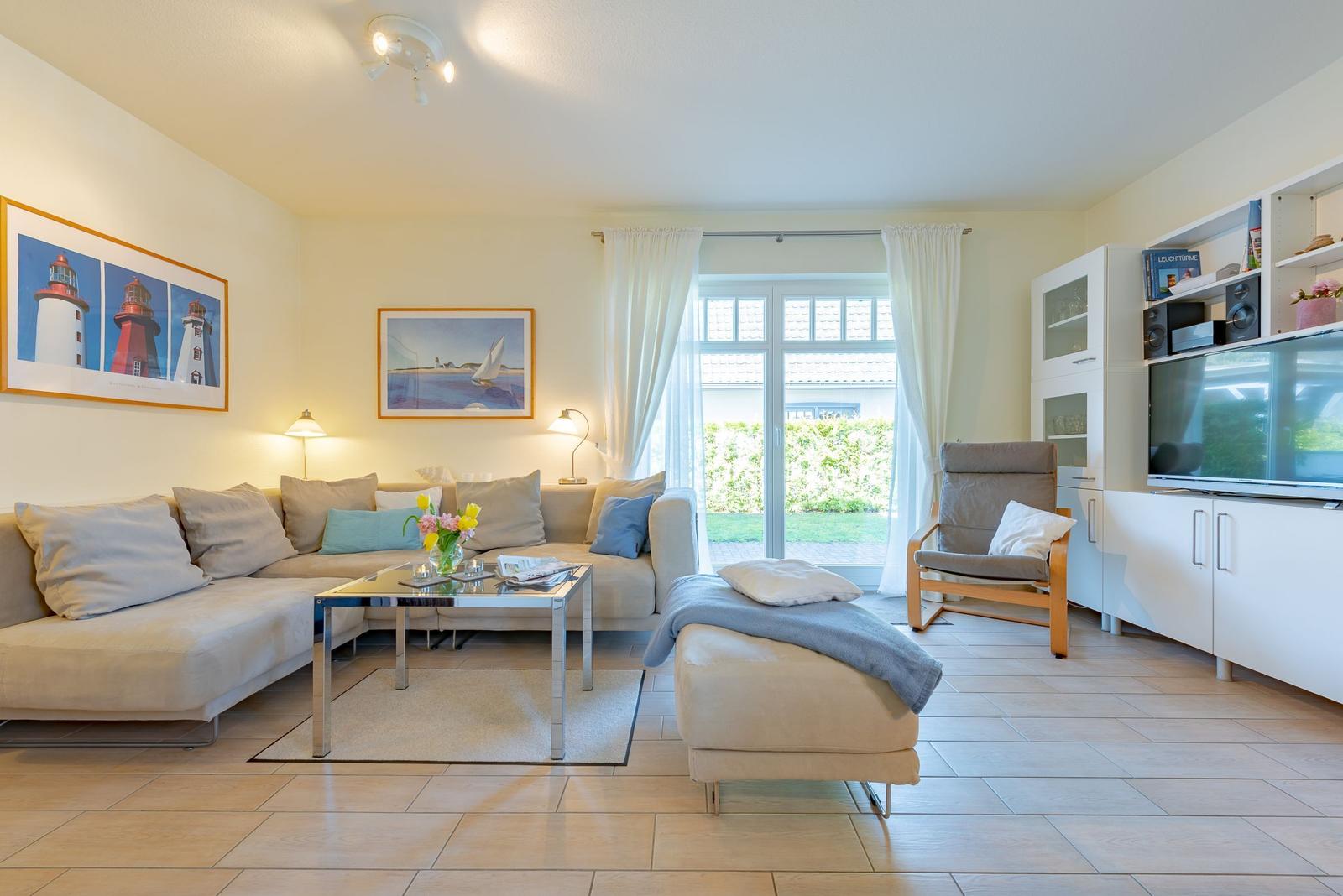 Wohnzimmer mit Sofa, Sessel, Couchtisch und TV. An der Wand hängen Bilder mit Leuchttürmen und Segelbooten.