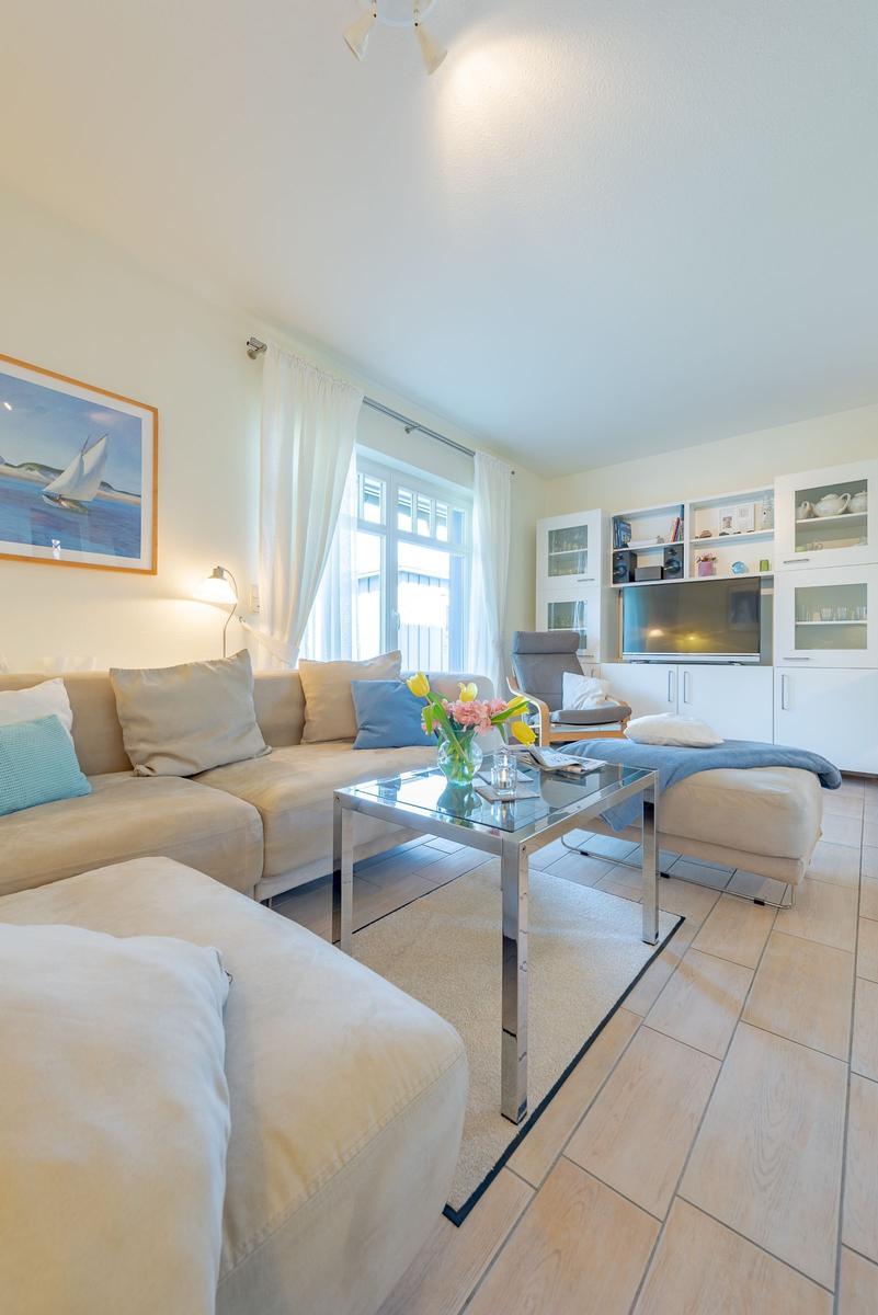 Wohnzimmer mit Sofa, Couchtisch und TV. Fenster mit weißen Vorhängen.
