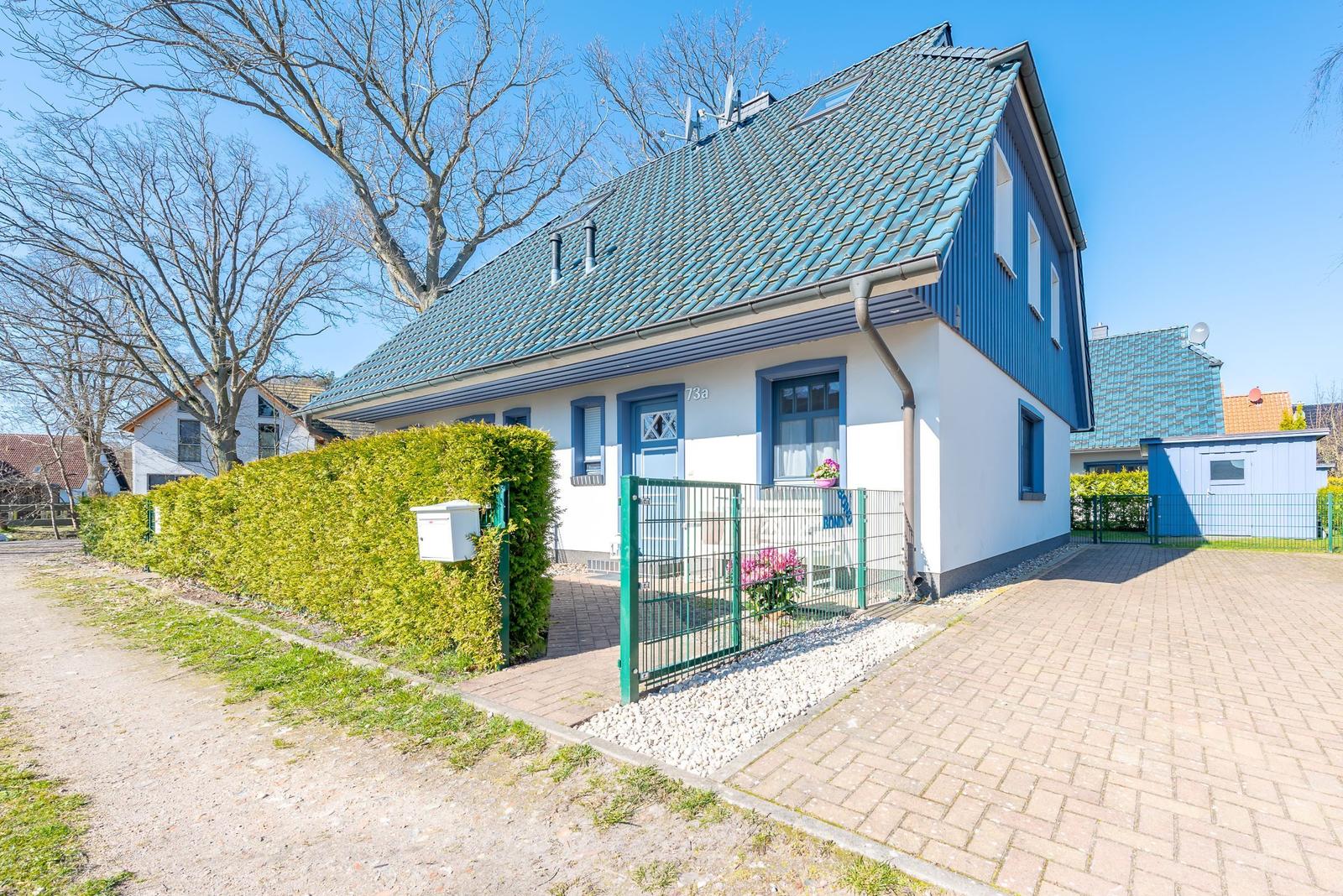 Ein Haus mit blauem Dach und weißen Wänden, umgeben von einem grünen Zaun und einem gepflasterten Hof.