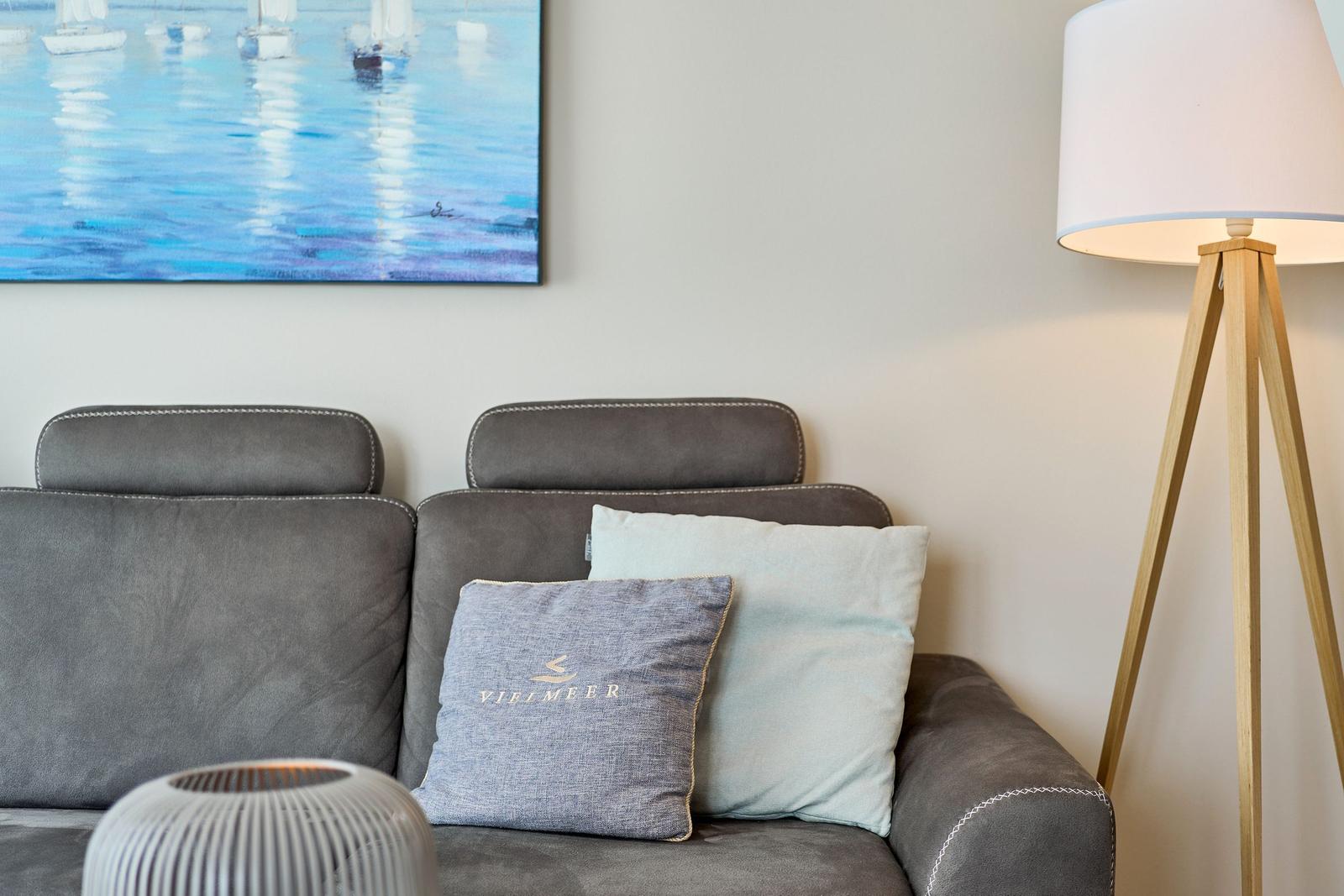 Graße Couch mit Kissen und Stehlampe neben Wandbild mit Segelbooten.