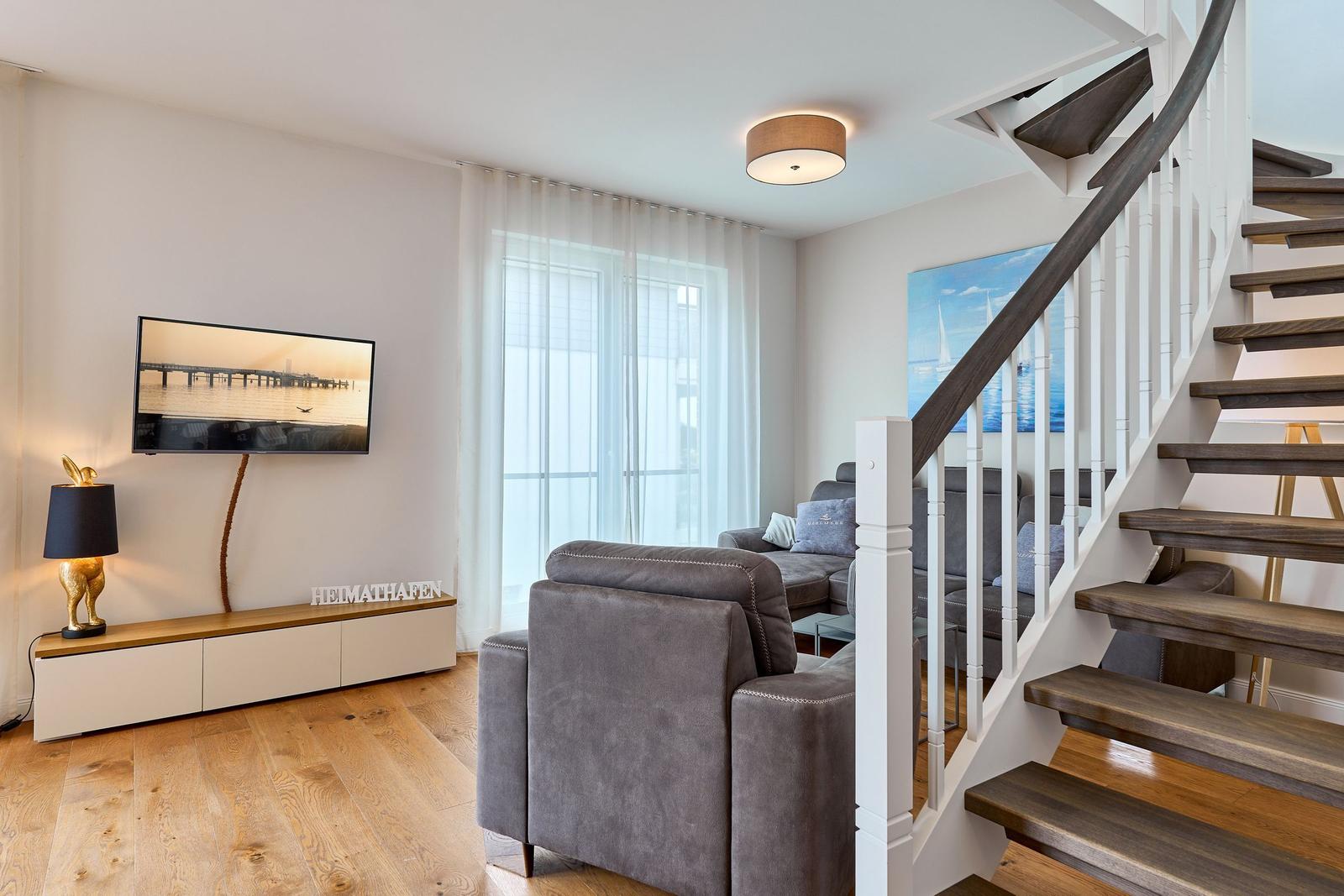 Wohnzimmer mit Sofa, Fernseher und Treppe.