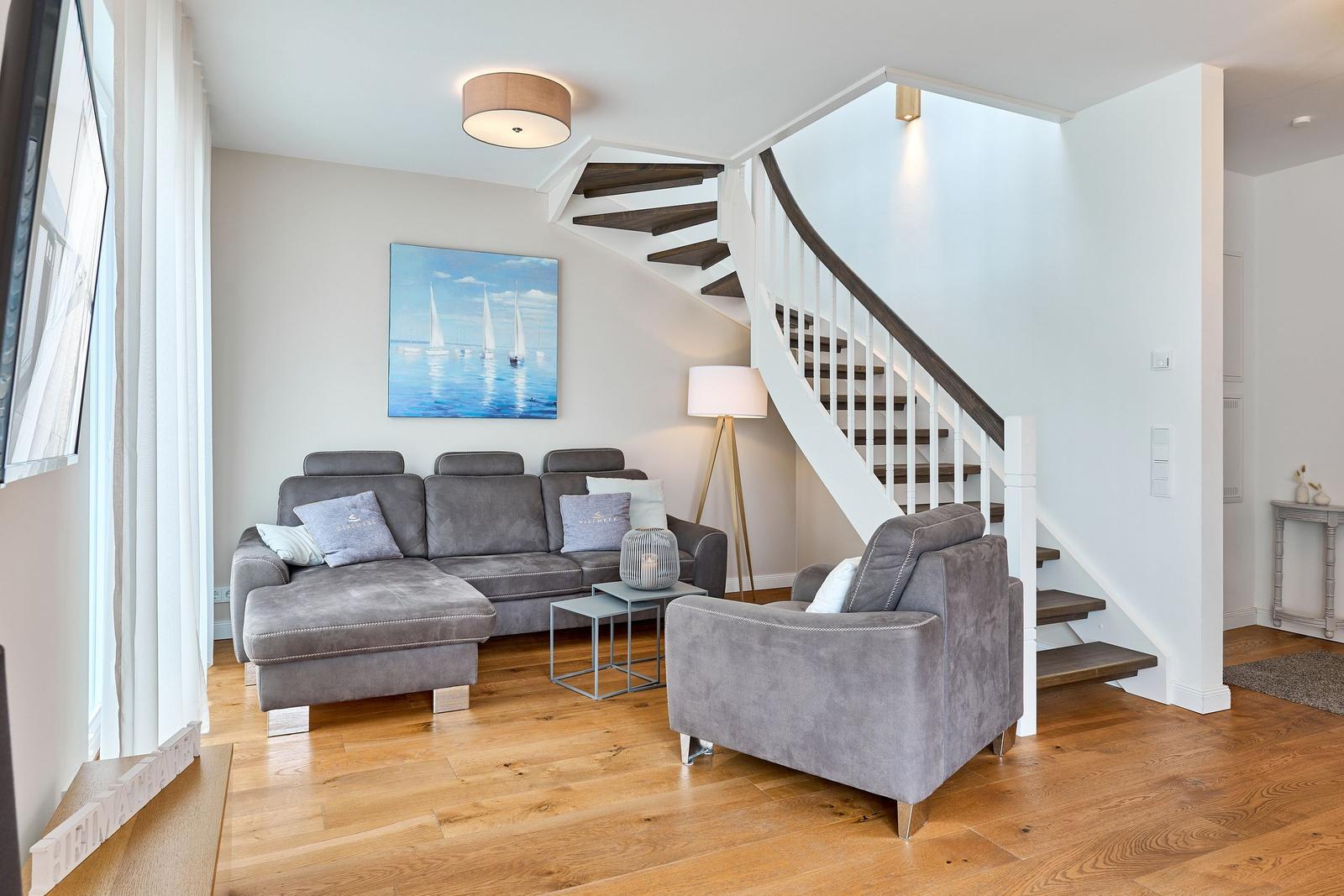 Wohnzimmer mit grauem Sofa, Treppenaufgang und Wandbild mit Segelbooten.