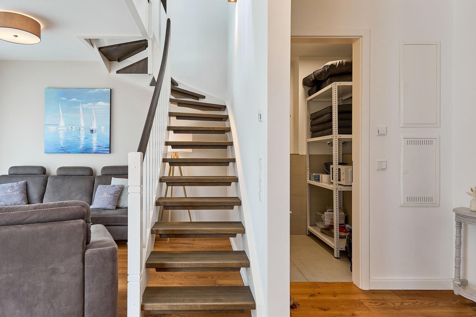 Treppenhaus mit Holzstufen führt zur oberen Etage. Wohnbereich mit Sofa und Wandbild.