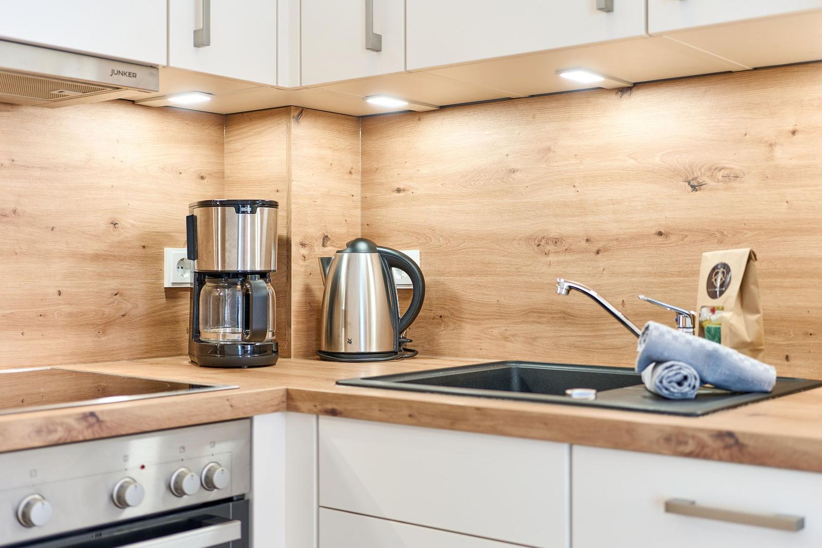 Küche mit Holzwand, Spüle, Kaffeemaschine und Wasserkocher.