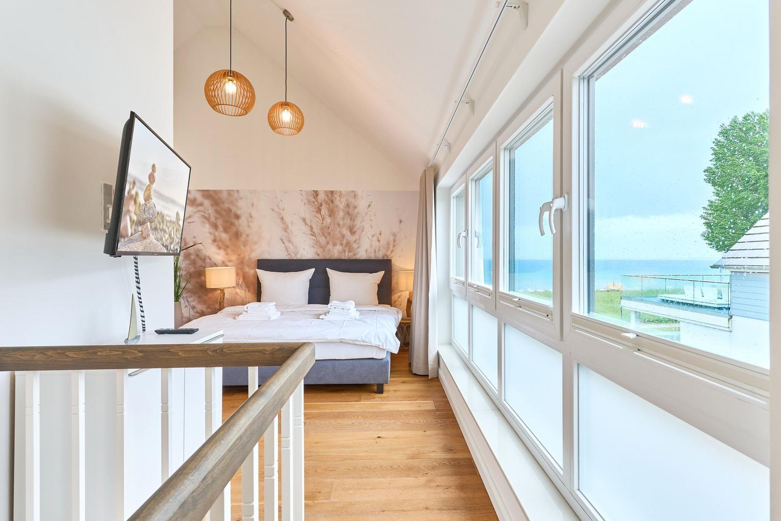 Schlafzimmer mit Blick aufs Meer, großes Fenster, Bett und TV.