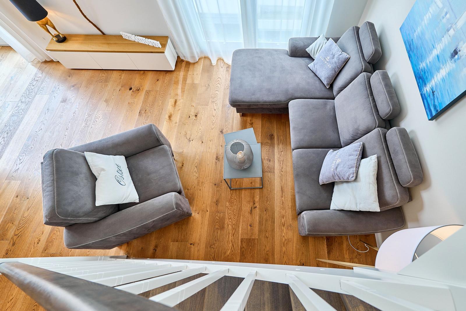 Ein Wohnzimmer mit grauem Sofa, Holzboden und Wandbild.