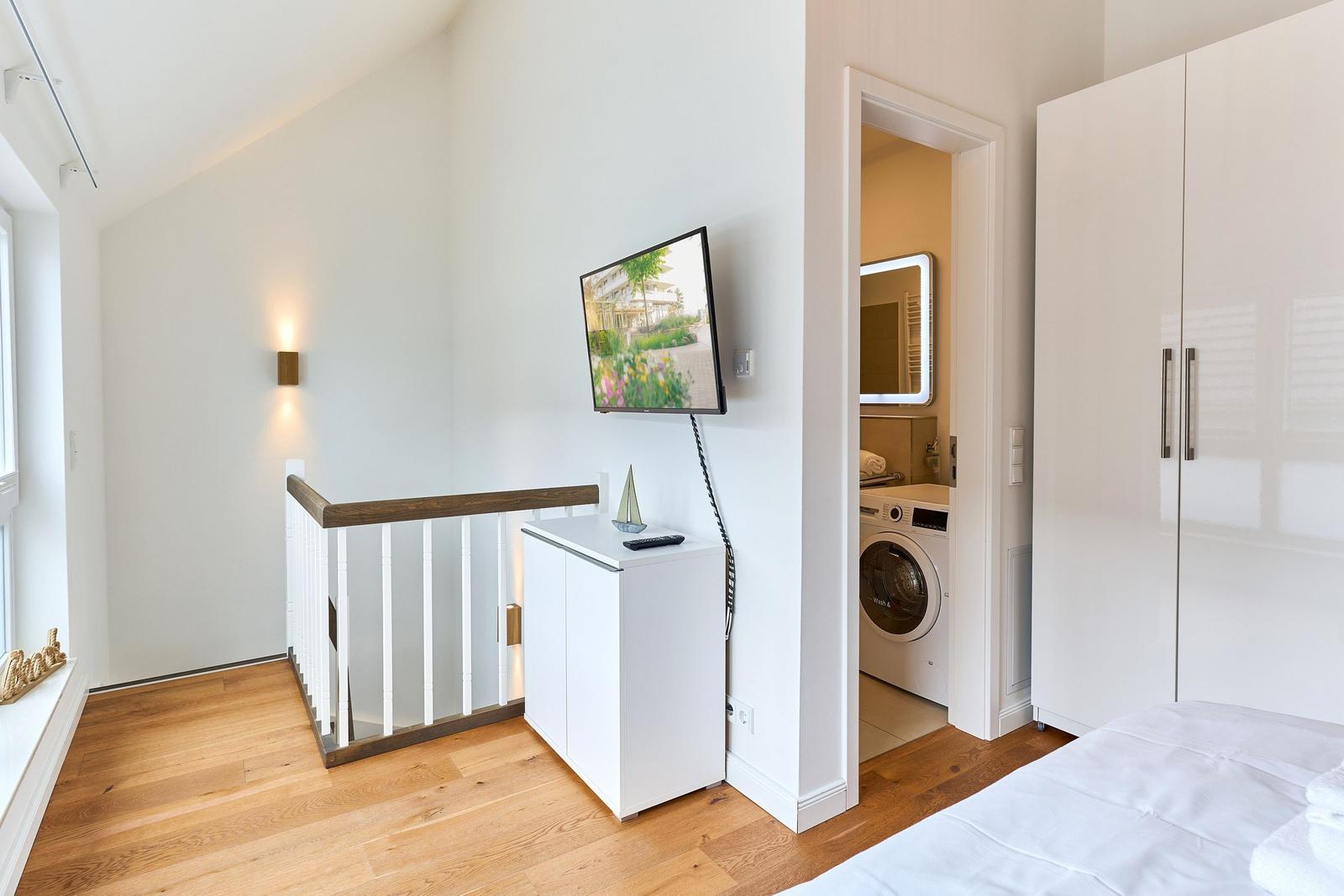 Schlafzimmer mit Bett, Kleiderschrank und TV. Blick in die Waschküche mit Waschmaschine.