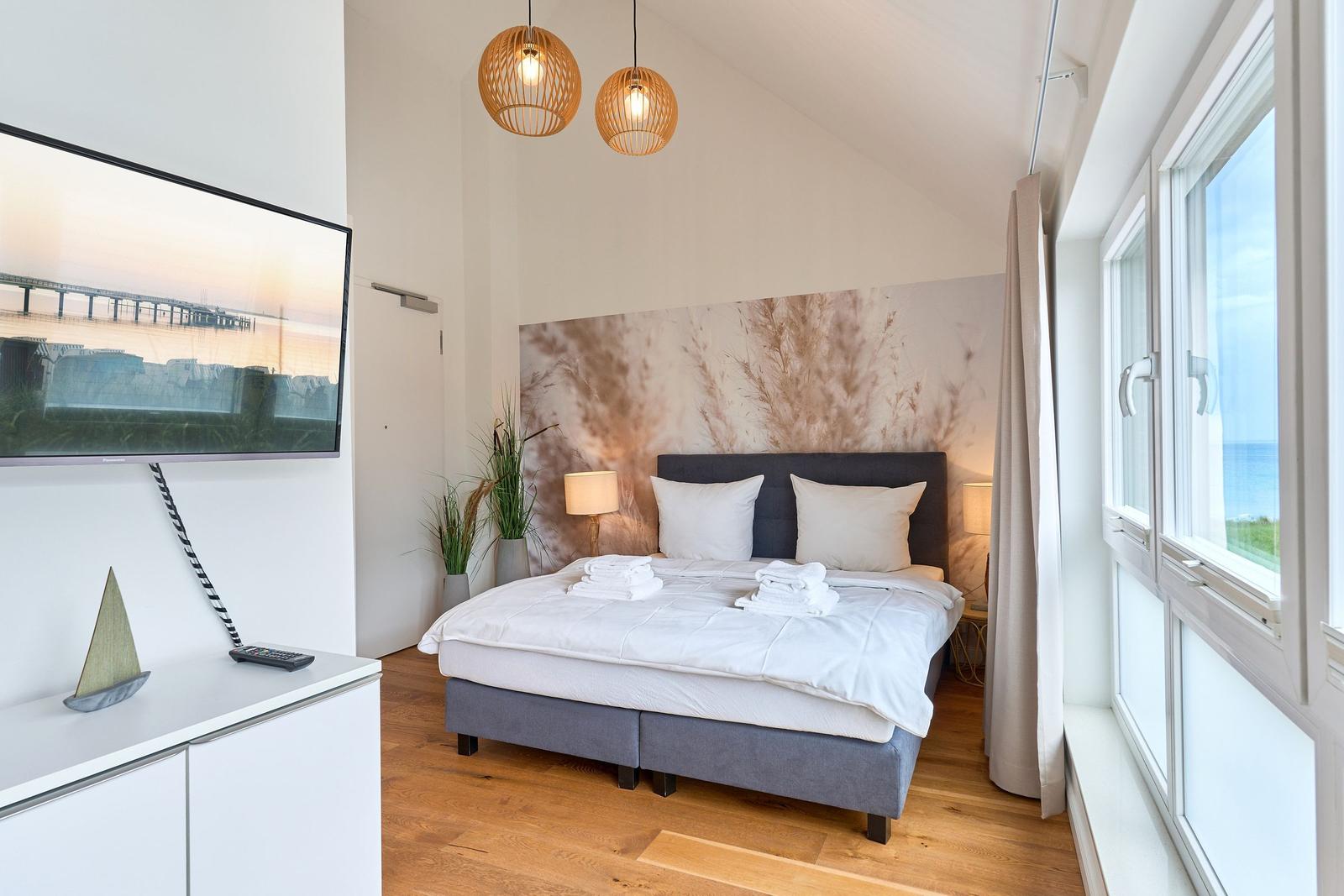 Schlafzimmer mit Bett, Fensterblick aufs Meer und Fernseher an der Wand.