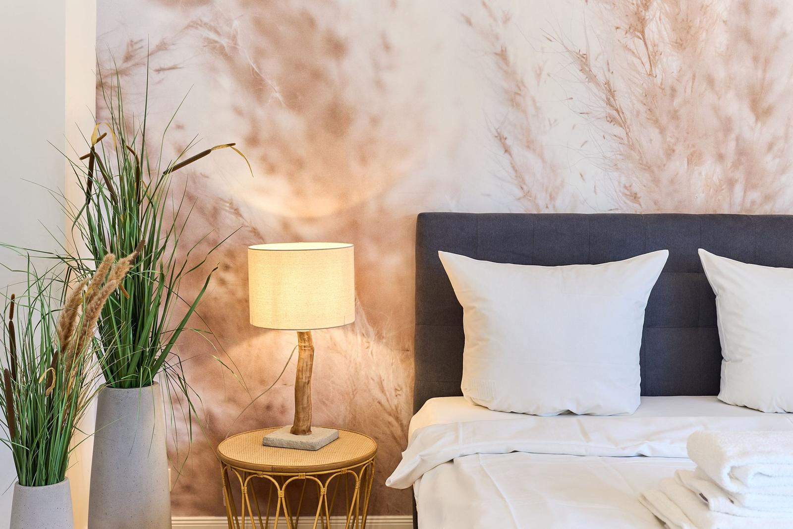 Schlafzimmer mit Bett, Nachttisch und Pflanzen an der Wand mit Muster.