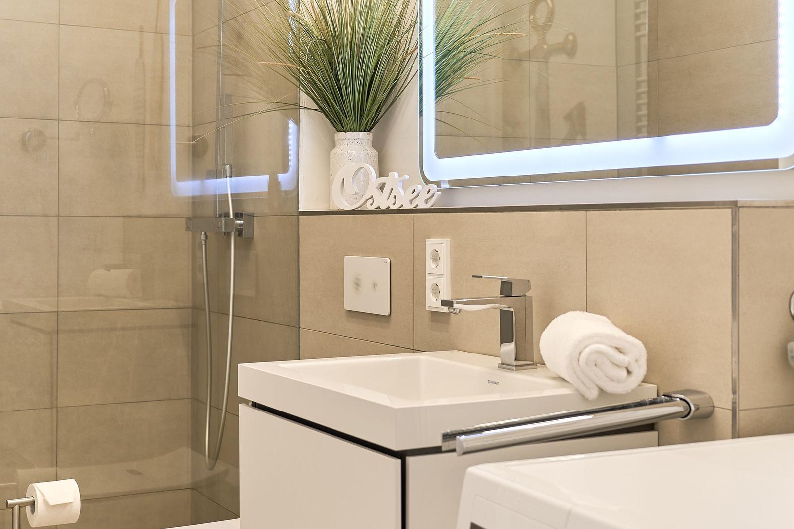 Bad mit Dusche, Waschbecken und beleuchtetem Spiegel.