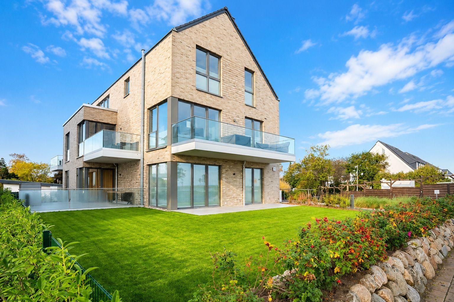 Moderne Villa mit Glasbalcony und grünem Garten unter blauem Himmel.