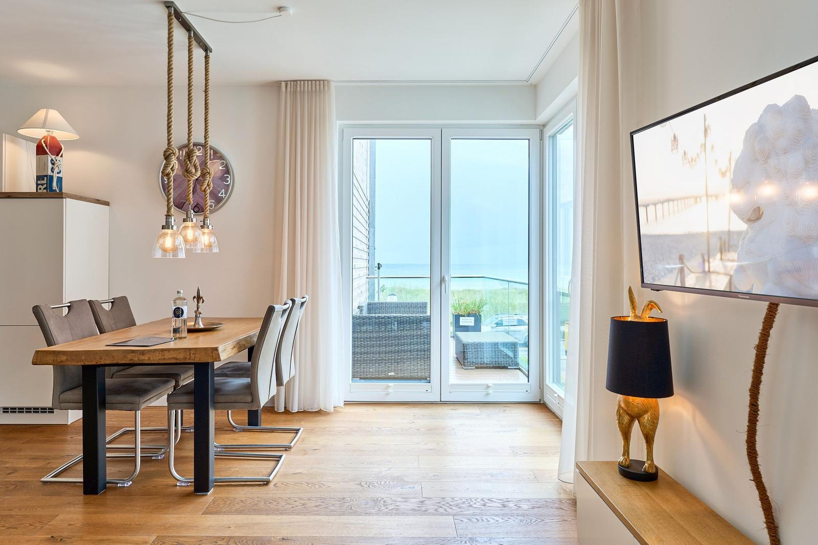 Esszimmer mit Tisch, Stühlen und Balkonansicht. TV und Lampe an der Wand.