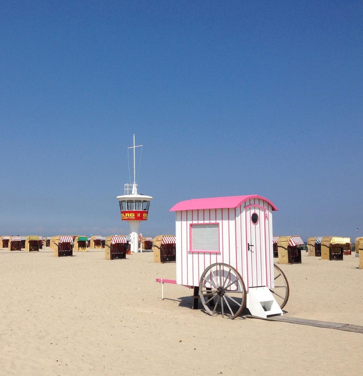 Strand mit Strandkörben und Wachturm unter blauem Himmel