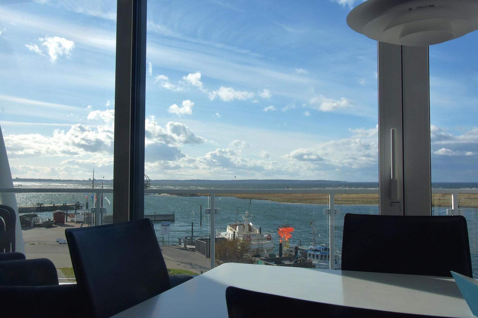Ein Essbereich mit Blick auf Hafen und Meer unter blauem Himmel mit Wolken.