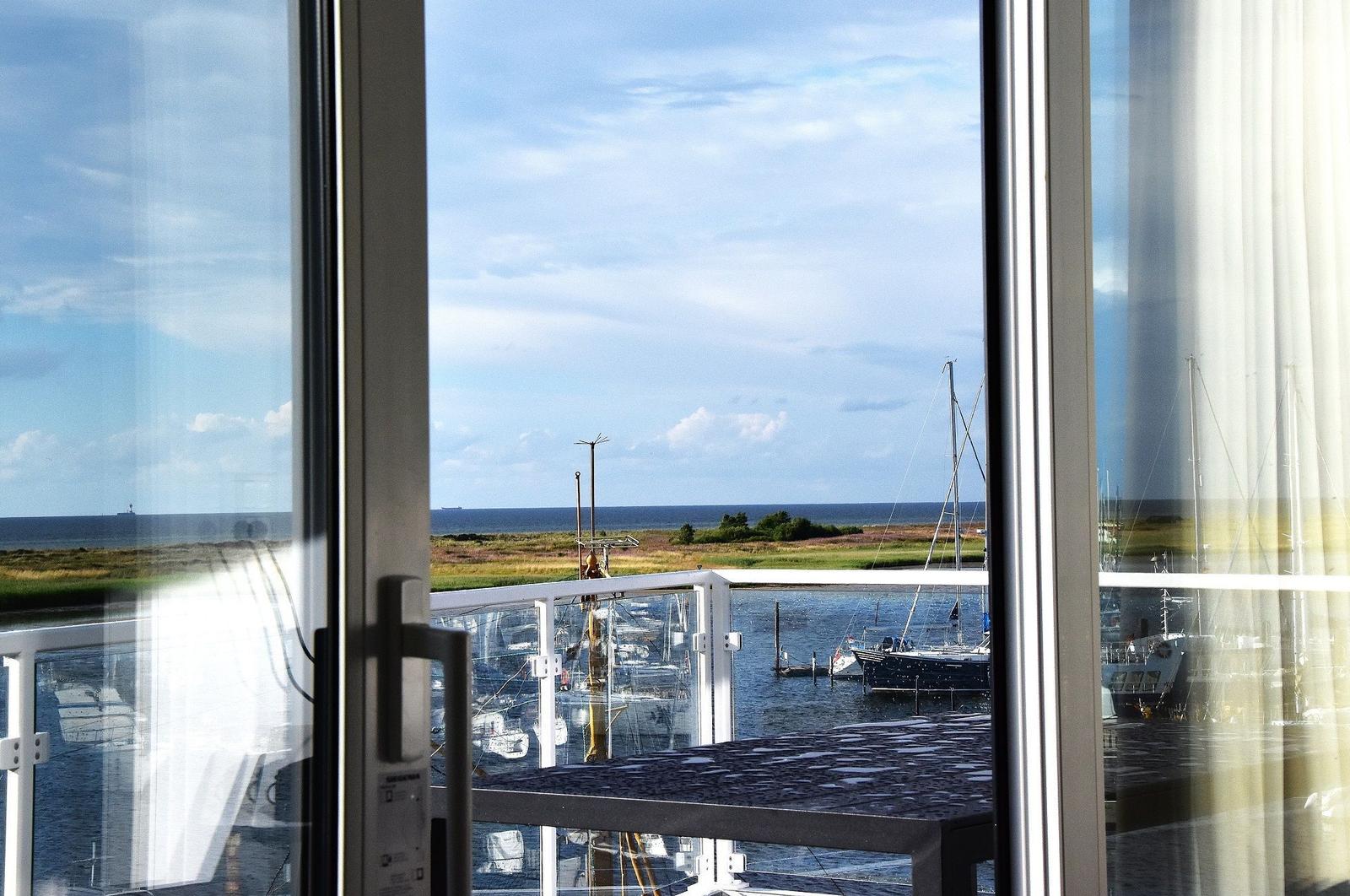 Blick auf Hafen mit Booten und Meer durch große Fenster