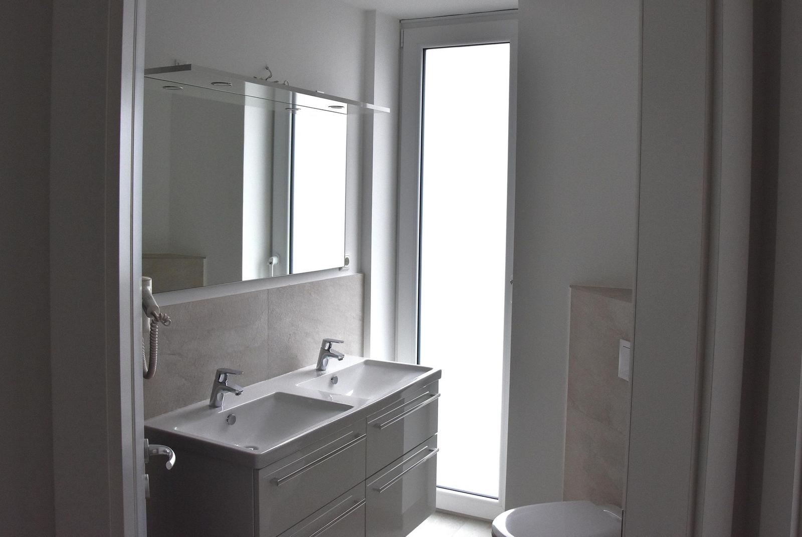 Badezimmer mit Waschbecken, Spiegel und Fenster.