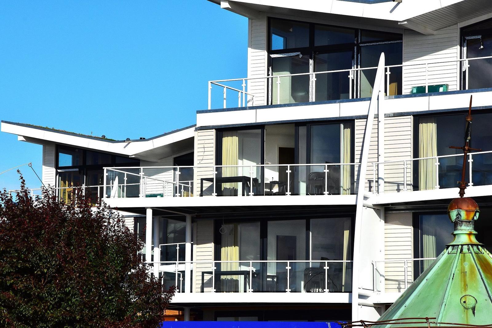 Modernes Mehrfamilienhaus mit Balkonen und großen Fenstern unter blauem Himmel.