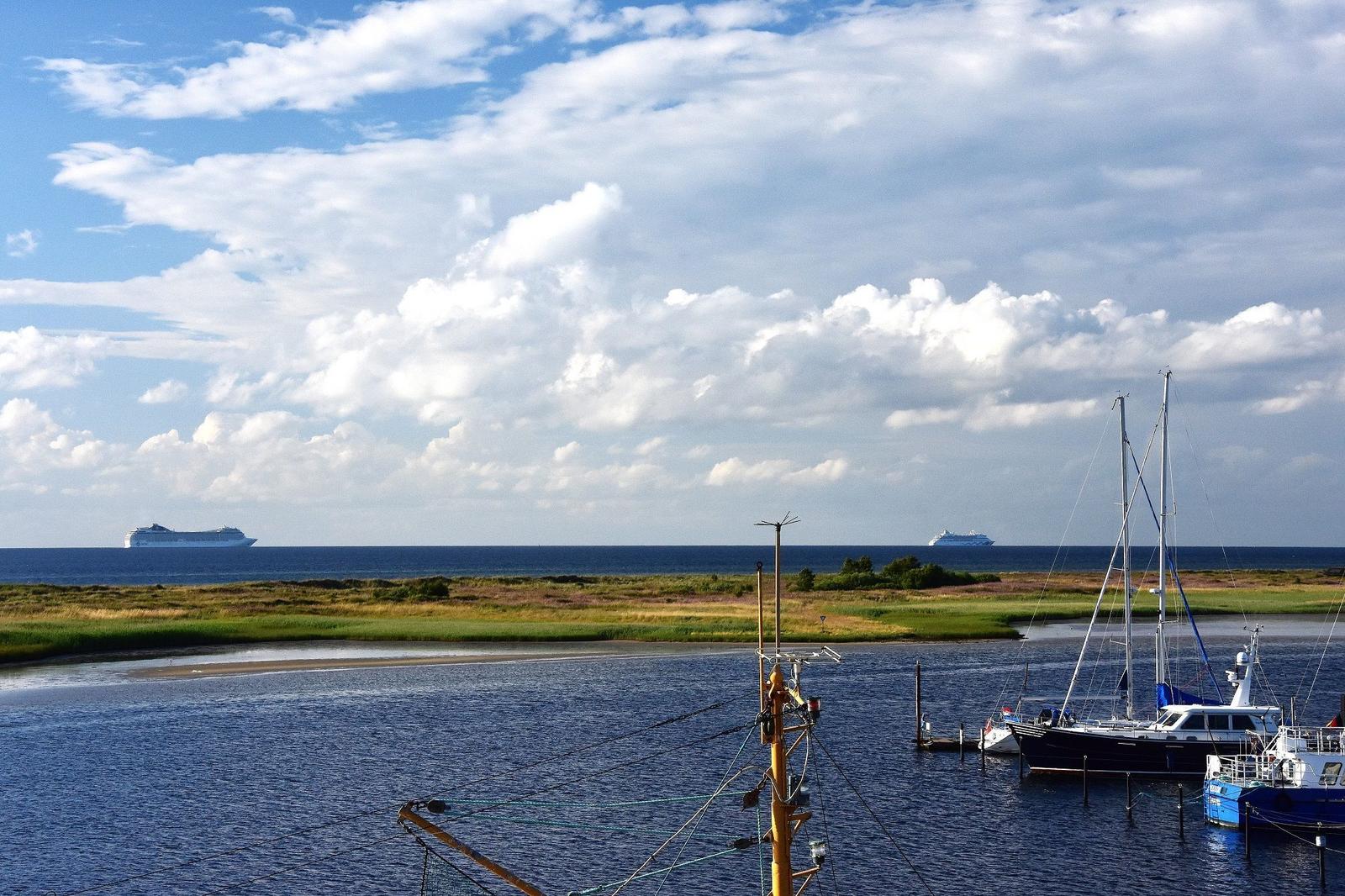 Hafen mit Booten und Blick auf zwei Kreuzfahrtschiffe im Meer.