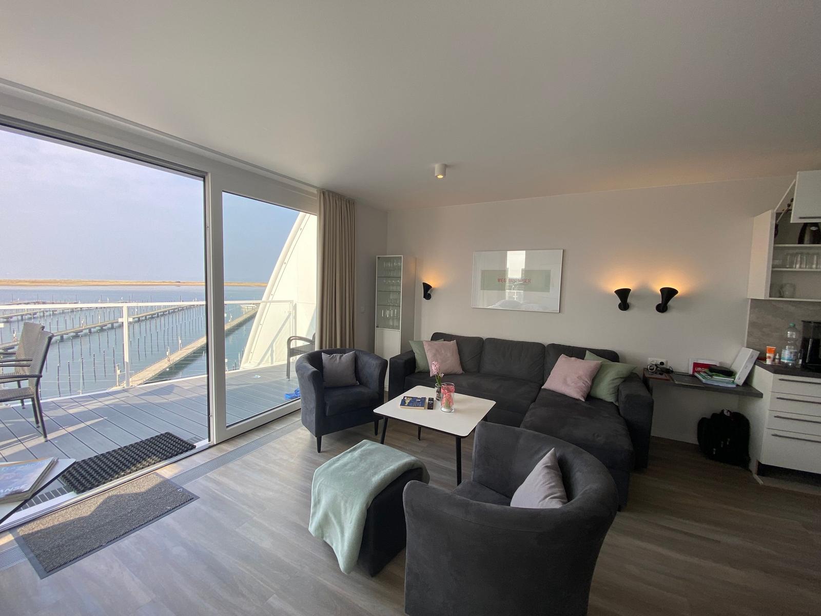 Wohnzimmer mit Sofa, Sesseln und Blick auf den Hafen.