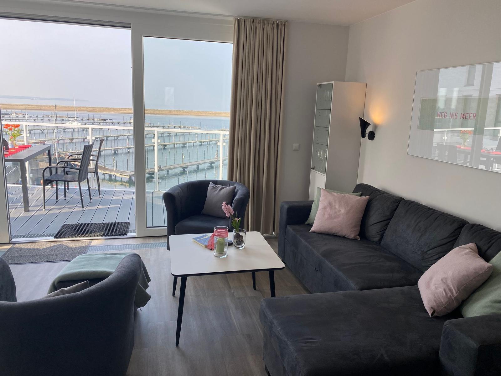 Wohnzimmer mit Sofa, Sessel und Tisch. Durchgang zur Terrasse mit Meerblick.
