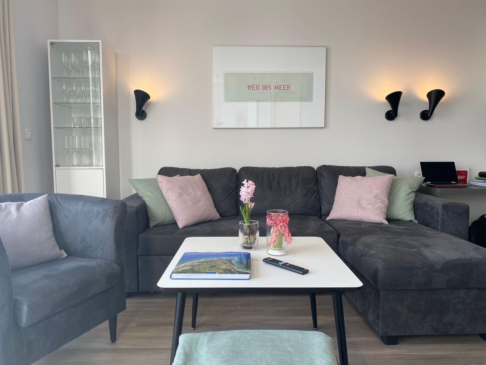 Ein Wohnzimmer mit grauem Sofa, Tisch und Wandbild.