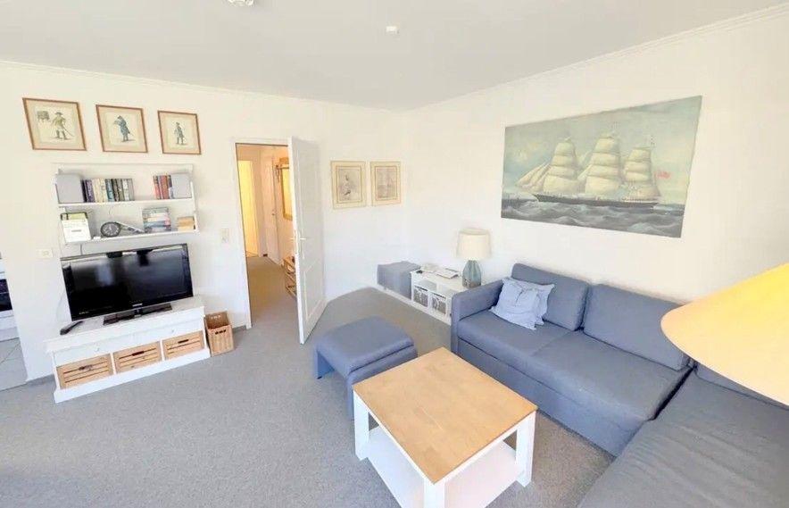 Wohnzimmer mit Sofa, Couchtisch und Fernseher. Wandbild zeigt Segelschiff.