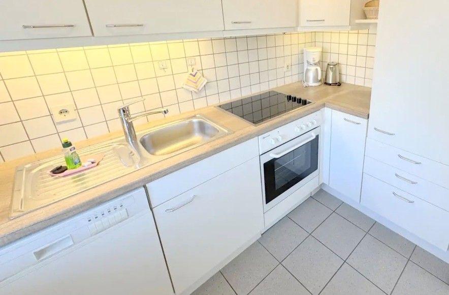 Küche mit weißen Schränken, Spüle, Herd und Waschmaschine.