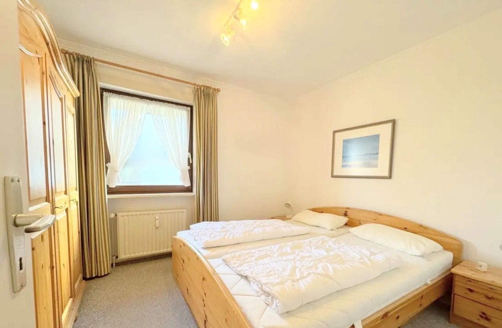 Schlafzimmer mit Holzbett, Kleiderschrank und Fenster mit Vorhängen.
