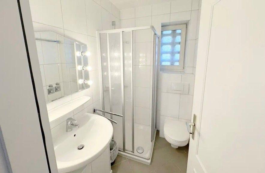 Badezimmer mit Dusche, Waschbecken und Toilette. Fenster mit Gitter.