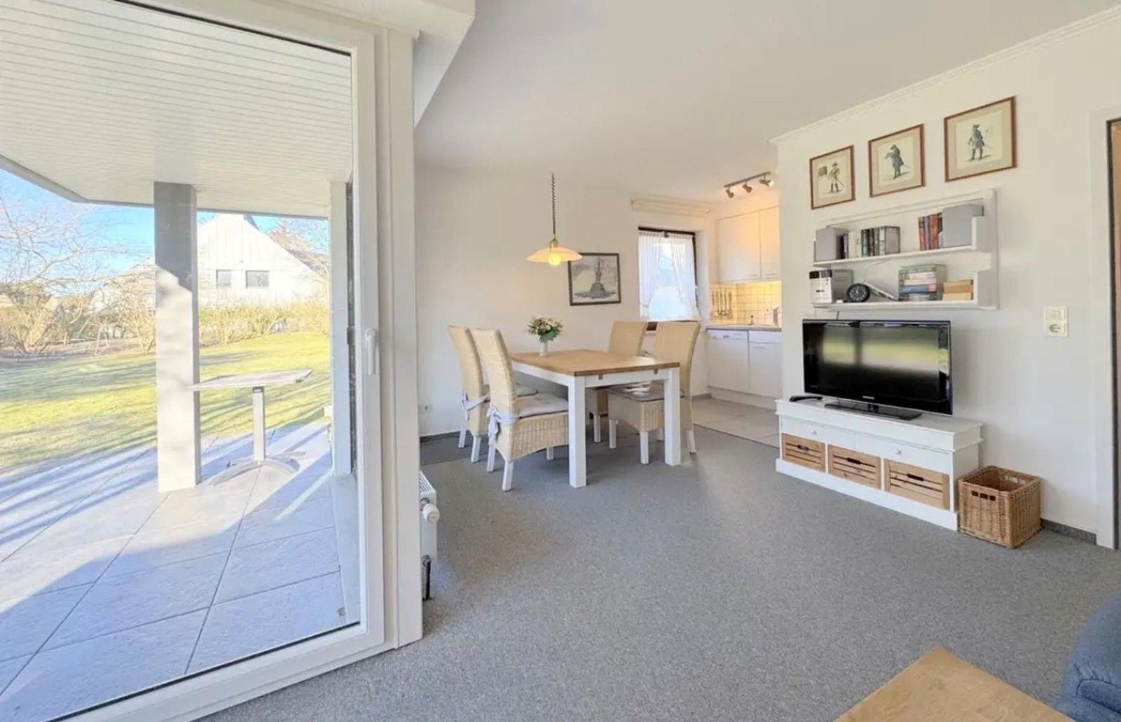 Wohn- und Essbereich mit TV, Tisch und Stühlen, Küche im Hintergrund, Terrasse mit Blick auf Garten.